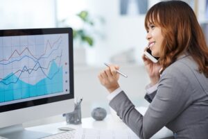 Young female entrepreneur talking on the phone when analyzing chart on computer screen