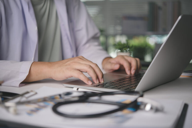 Doctor typing on a laptop at a desk with a stethoscope, reviewing their practice’s AI search visibility online